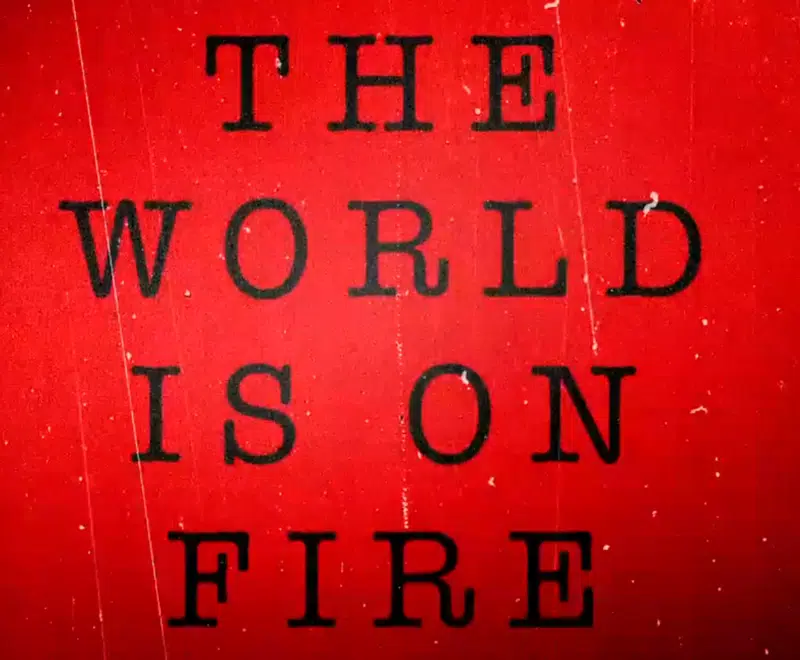 Thumbnail for the Dead Dog in a Suitcase Asylum trailer. The words 'THE WORLD IS ON FIRE' are positioned centrally in a large black font. This text fills most of the image. There is a vibrant red background behind the text which features small static elements such as thin white lines and dots.
