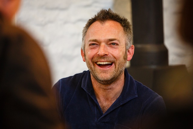 A smiling man with stubble engaging in conversation.