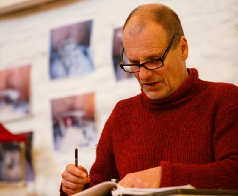 Man in red sweater focusing intently on writing in a notebook.