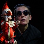 Performer with sunglasses presenting a puppet in red costume.