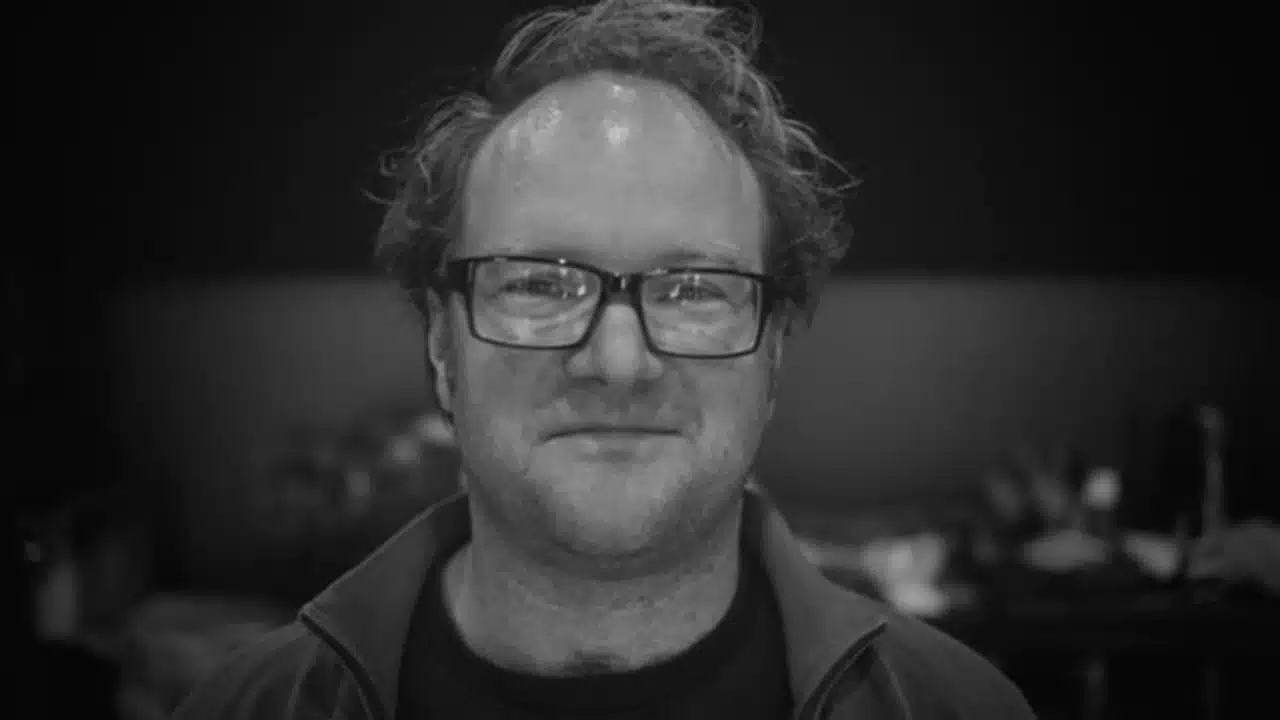 Black and white portrait of a smiling man with glasses.