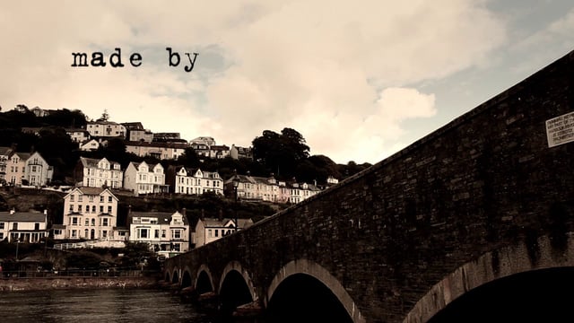 Stone bridge with arches leading to a hillside town under a cloudy sky.