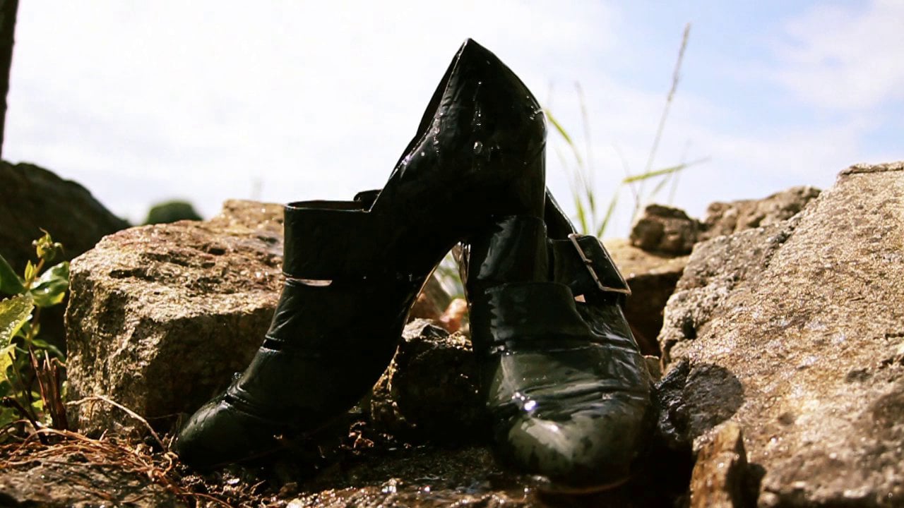 A pair of black high-heeled shoes abandoned on a rugged terrain under a bright sky.