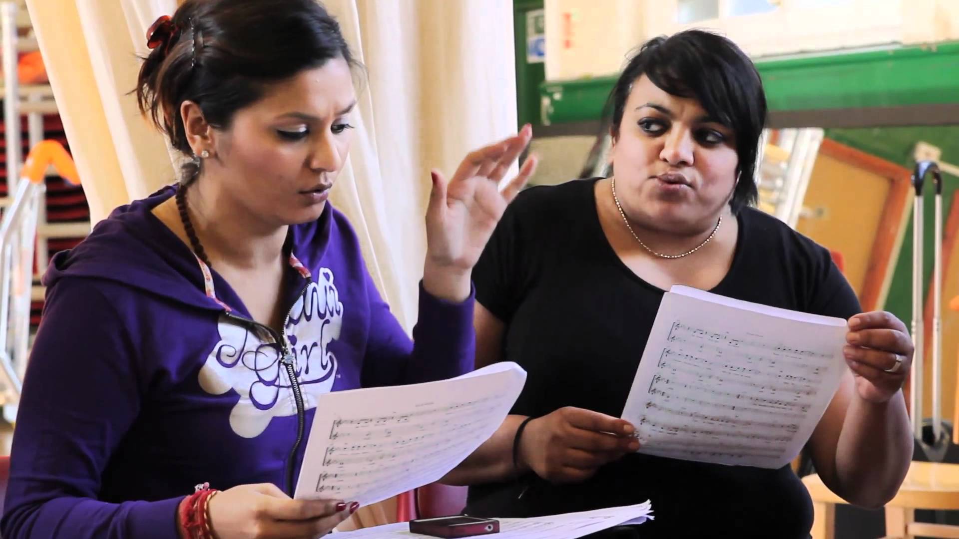Two women engaged in a discussion over a sheet of music.