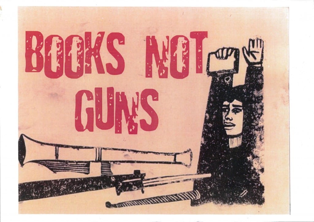 Fly poster for Dead Dog in a Suitcase. Design features a figure dressed in a black top, with their arms raised. In their right hand they are holding a book. To the left, there is a gun pointing towards the figure in a threatening manner. At the top of the image are the words 'Books not guns' written in red or dark pink. The lettering is all in capitals but the letters are uneven and the ink is missing in places. The poster has a pink background.
