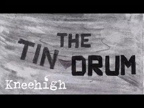A thumbnail for the Tin Drum teaser trailer. The background and text are drawn by a pencil. The text reads 'The Tin Drum' and is drawn in heavy black pencil marks with some overlapping on the edges. The background has been shaded in my a lighter pencil and is mostly grey.