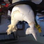 An upside down image of a sculpture of a bird made out of paper in a cluttered room. Books, utilities and general household items can be seen in the background.