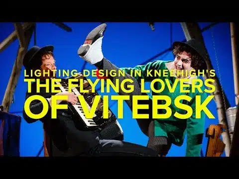 Thumbnail for a video interview on lighting design in the Flying Lovers of Vitebsk. Bold yellow text in the foreground reads 'Lighting Design in Kneehigh's Flying Lovers of Vitebsk' Behind this text are two players, one holding an accordion and the other with their leg held in the air. Both individuals are in costume and are standing in front a well lit blue background with wooden posts.