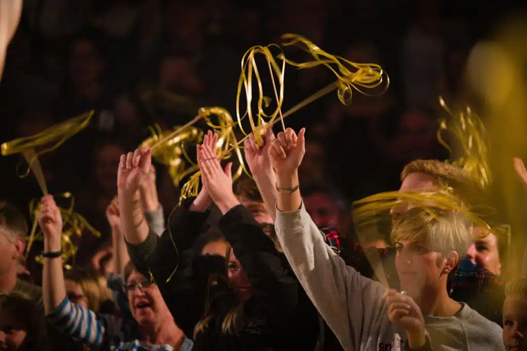 Photograph of Kneehigh's performance of Ubu at the Asylum in 2019. Image features the audience waving gold ribbons in the air and clapping.