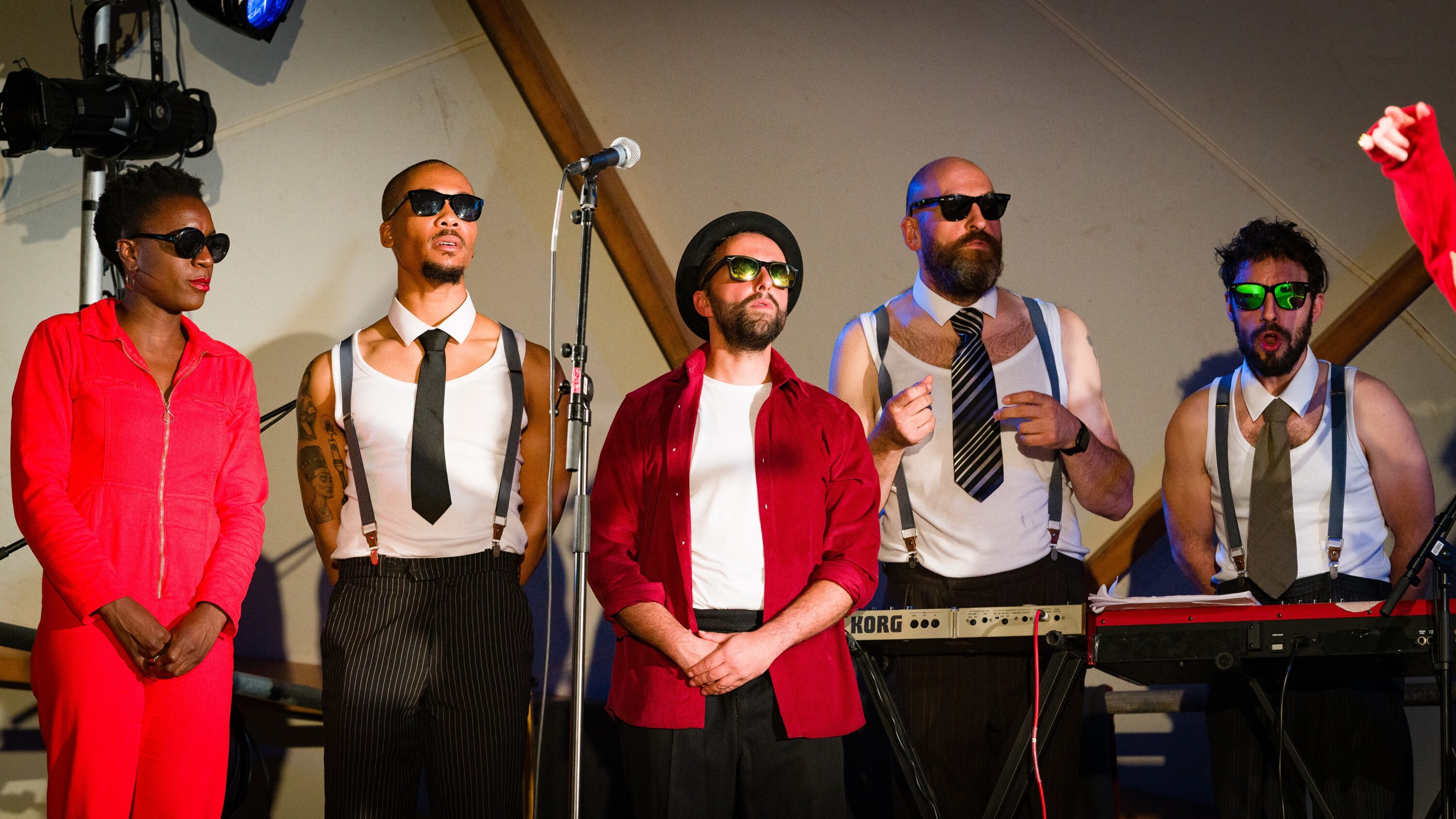 Photograph from Kneehigh's Ubu. The image features 'The Sweaty Bureaucrats band' standing on stage dressed in red, white and black with sunglasses.
