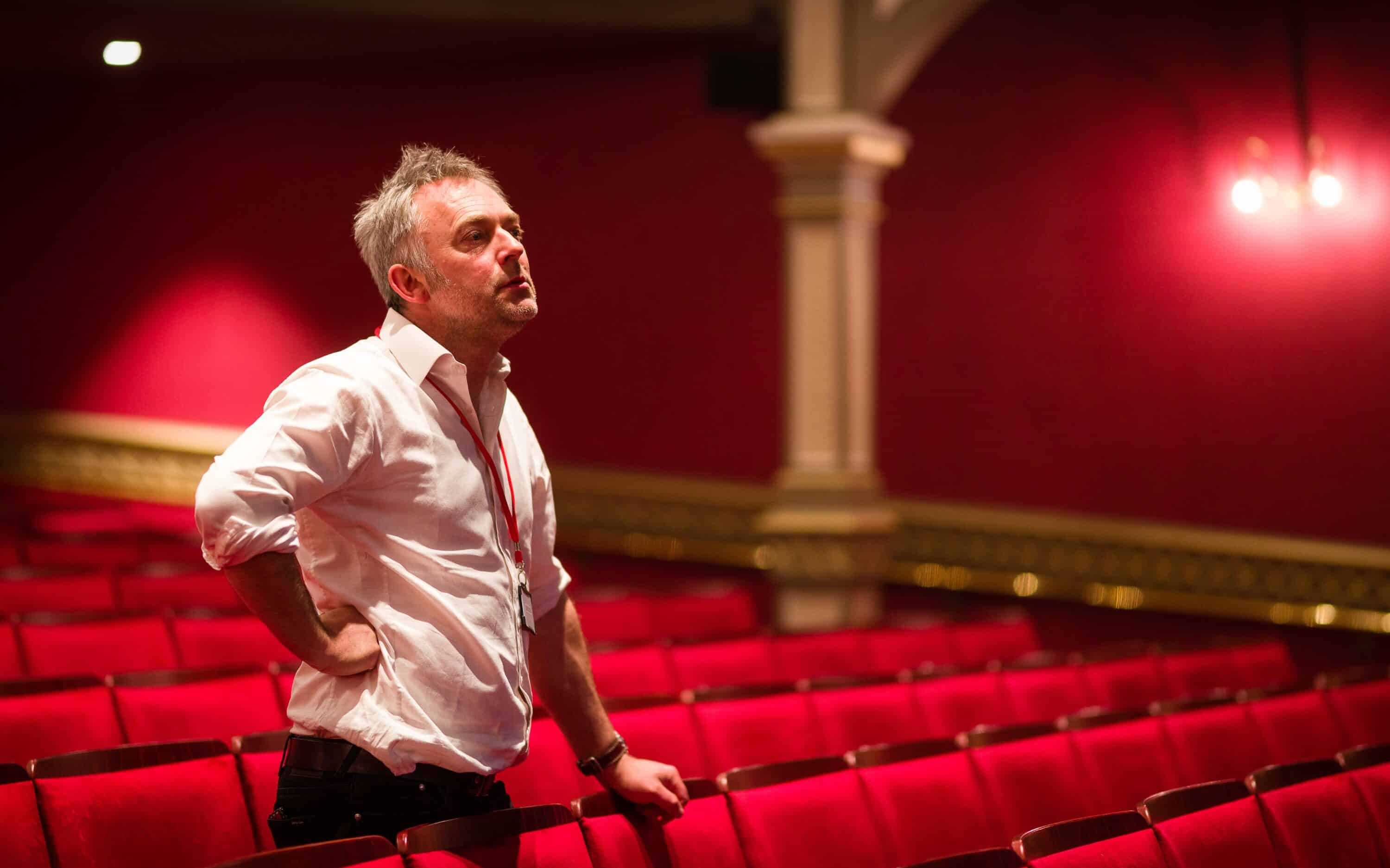 Featured image for Kneehigh's Ubu. Image features music director Charles Hazlewood standing in theatre amongst rows of red seats.