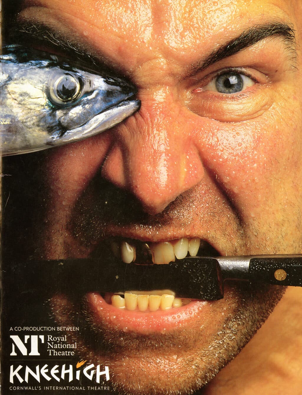 Programme features a close set photograph of a man's face. His right eye is obscured by the head of a mackerel and he holds a knife between his teeth - one of which is gold. His composure appears angry.