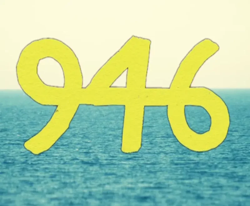 The numbers '946' are presented in a curved font in bright yellow. This is set against the backdrop of an ocean horizon.
