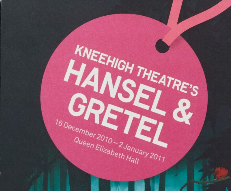 The image contains a portrait illustration of two cartoon figures standing in a dark green forest with some rabbits at their feet. There is a bright red house in the distance. A large pink circle resembling a gift label is presented in the top centre of the image and contains white text that reads 'Kneehigh Theatre's Hansel and Gretel 16 December 2020 - 2 January 2011 Queen Elizabeth Hall.