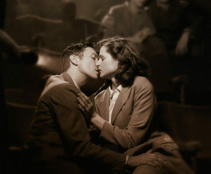 Image features two individuals, one male and one female, embracing romantically in a cinema. The backdrop is blurry. Bold white text in the bottom left of the image reads 'Brief Encounter'. Smaller pink text reads 'Adapted and Directed by Emma Rice'.